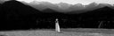 Person in a white hat and long dress standing in a field with mountains in the background
