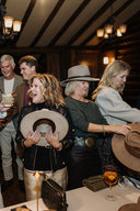 Group of people gathered around a table in a dimly lit room, holding hats.
