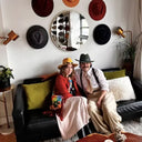 Two people sitting on a couch with hats displayed on the wall behind them.