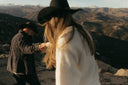 Two people in hats standing on a mountain with scenic views