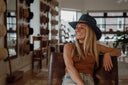 Woman sitting on a leather chair wearing a blue hat in a store with hat displays.