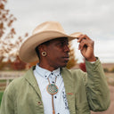 Person wearing a beige cowboy hat and green jacket in an outdoor setting