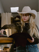 Person wearing a cowboy hat while shaping another hat with steam iron