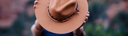 Person holding a brown hat against a blurred natural background