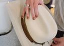 Beige handbag with brown handle held by a person, blurred background