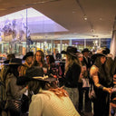 Group of people wearing cowboy hats in a modern indoor setting with large windows.