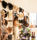 People in a room with a hat rack on the wall and bottles on a table.