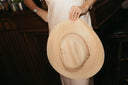 Person holding a straw cowboy hat with a blurred background