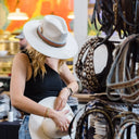 Woman holding a white hat with various hats on display