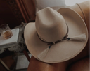 Beige cowboy hat with decorative band held by a person, blurred background