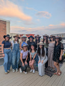Group of women in hats posing on a rooftop with a scenic background